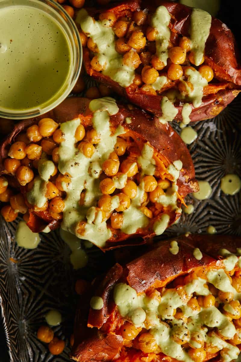 A close up of roasted chickpea stuffed sweet potatoes with cilantro garlic cashew sauce.