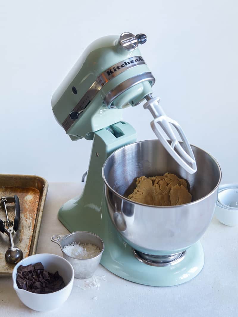 Cookie dough in a mint colored Kitchen Aid stand up mixer with baking accessories.