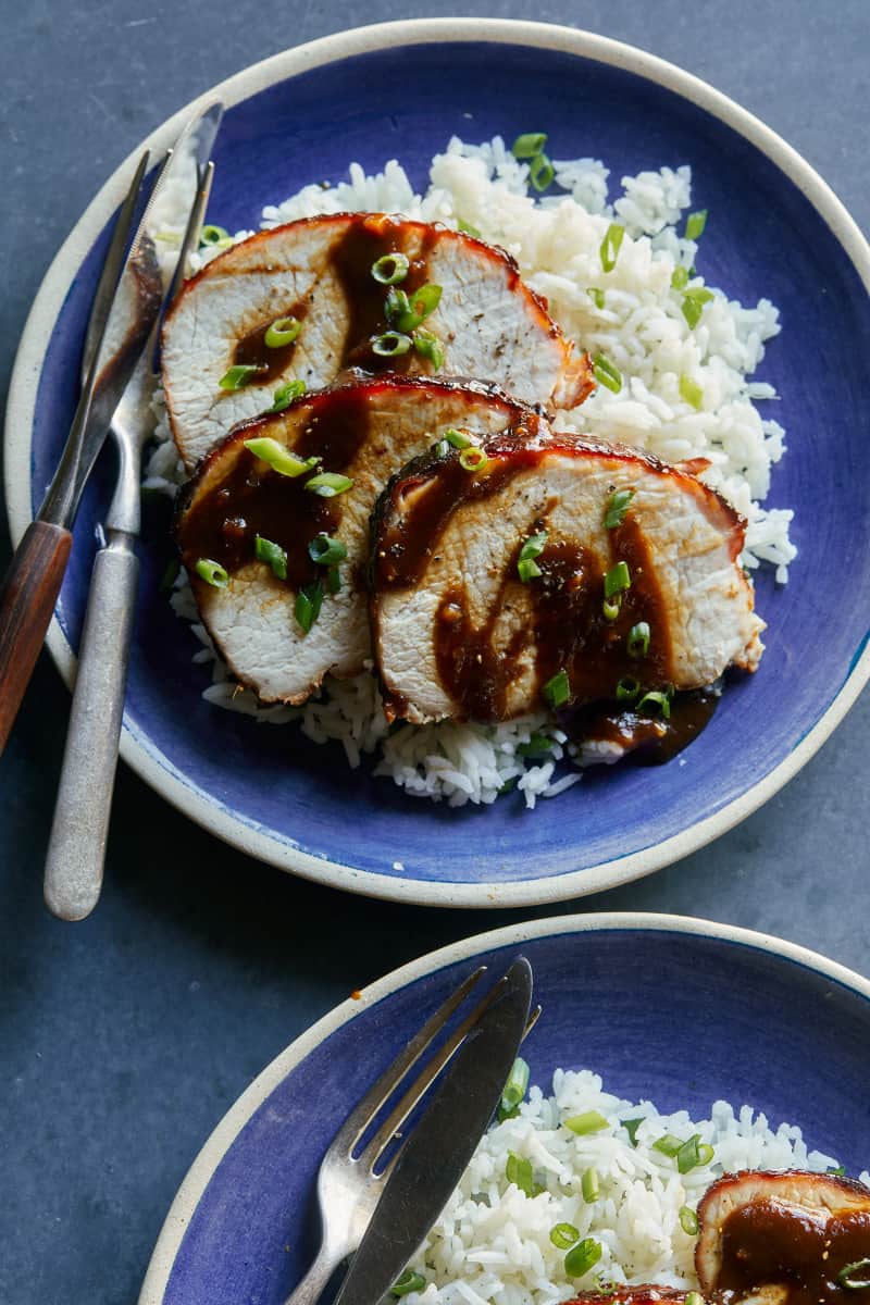 A plate of sliced char siu pork tenderloin over white rice and a fork and knife.