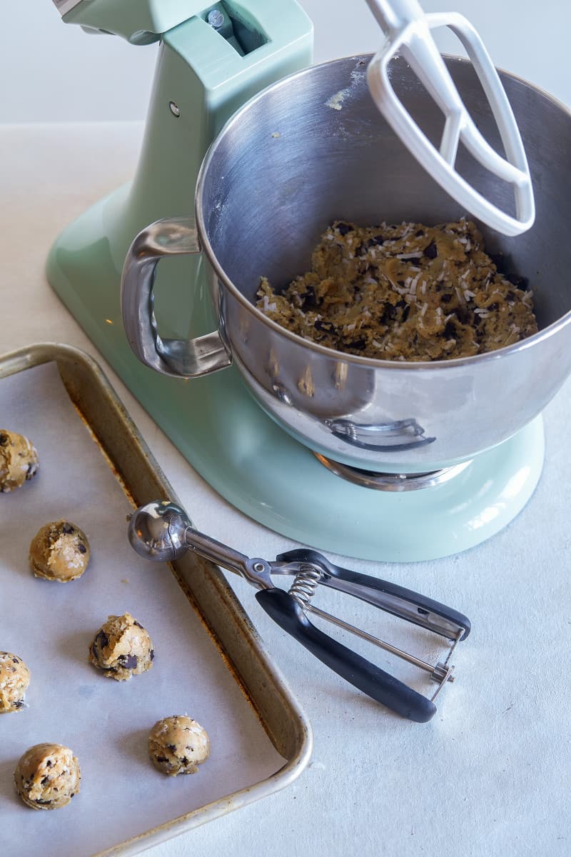 Cookie dough in a Kitchen Aid stand up mixer and on a baking sheet with a scoop.