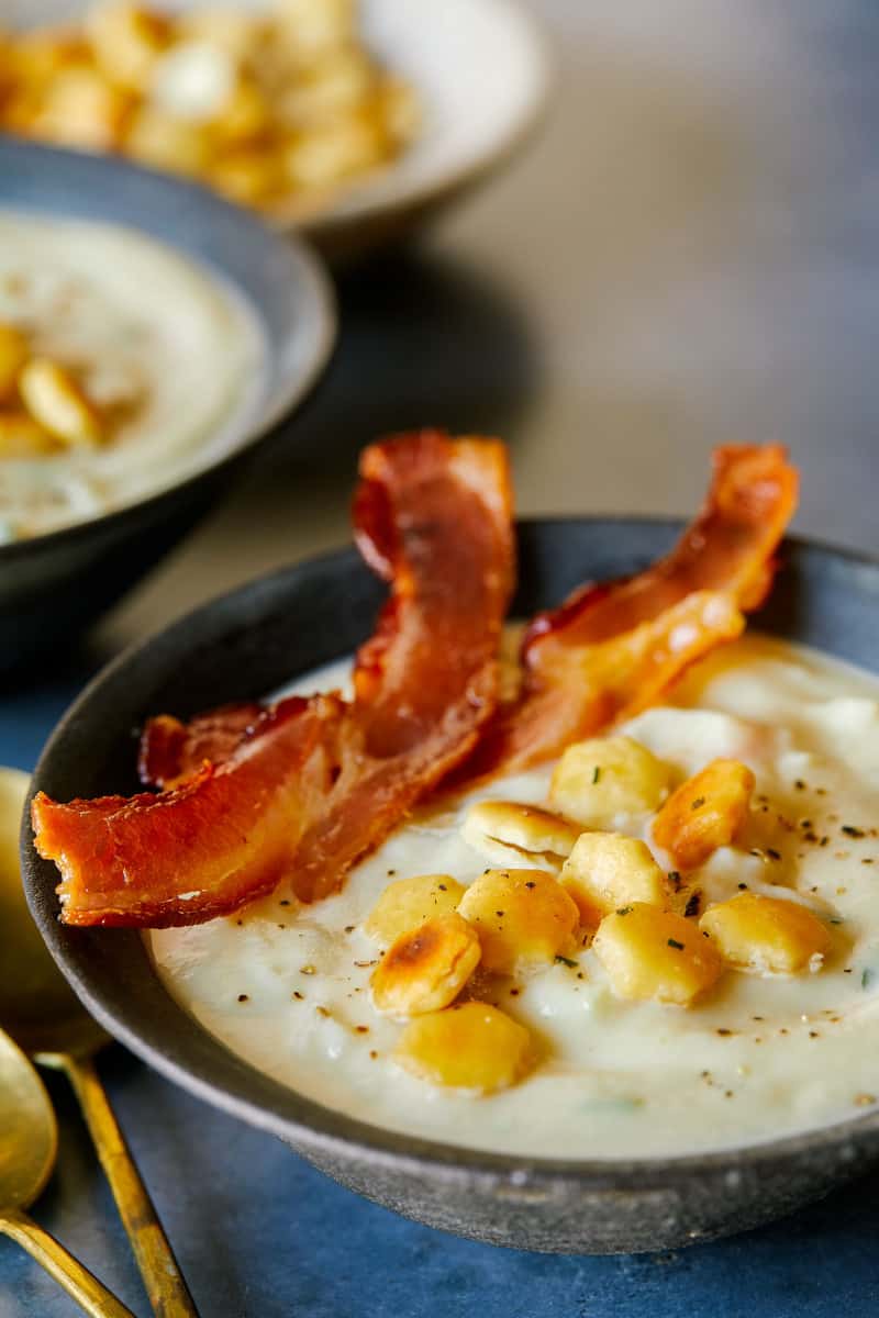 A close up of a bowl of creamy vegan cauliflower chowder with crackers and bacon.