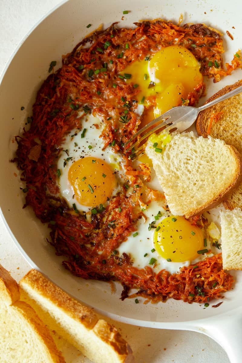 A close up of cheesy skillet sweet potato hash browns and eggs with a fork.