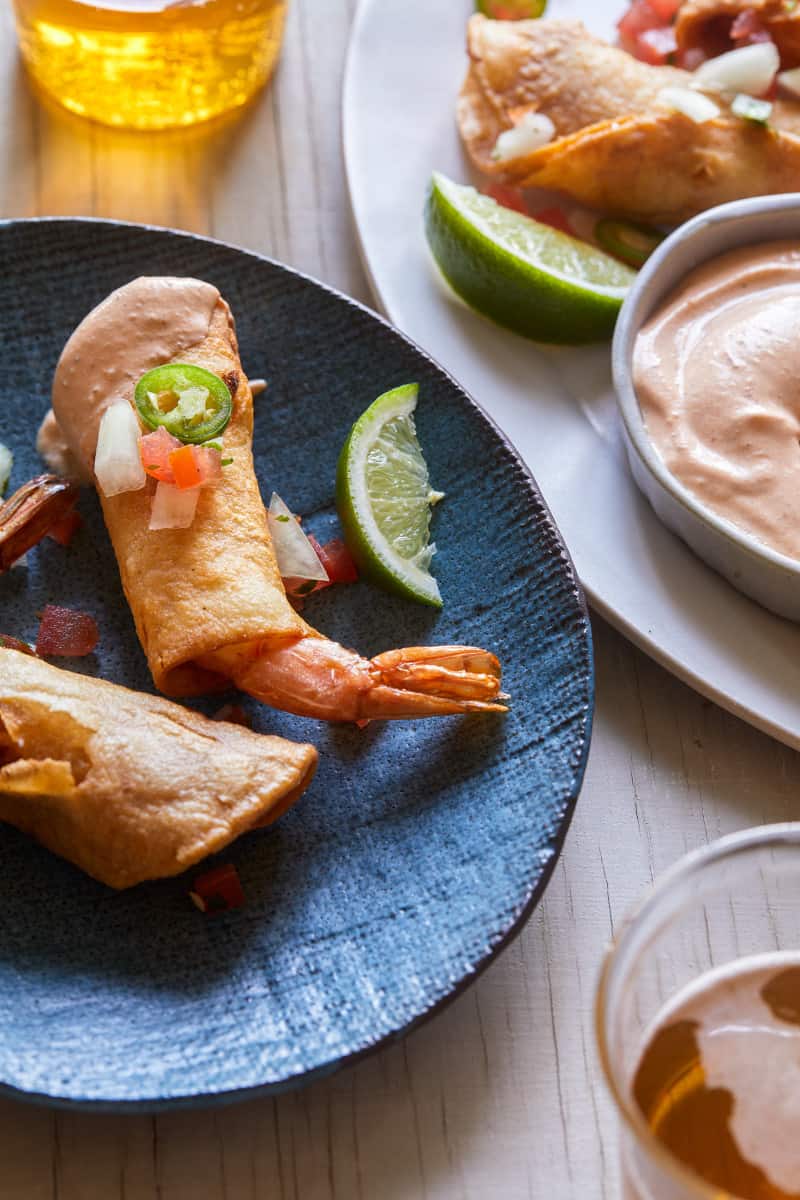 A close up of shrimp taquitos with lime wedges and creamy chipotle sauce.