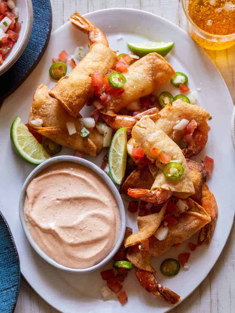 A platter of shrimp taquitos with lime wedges and creamy chipotle sauce on the side.