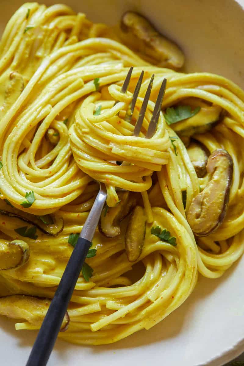 A close up of Thai yellow curry noodles with shiitake mushrooms twirled on a fork.