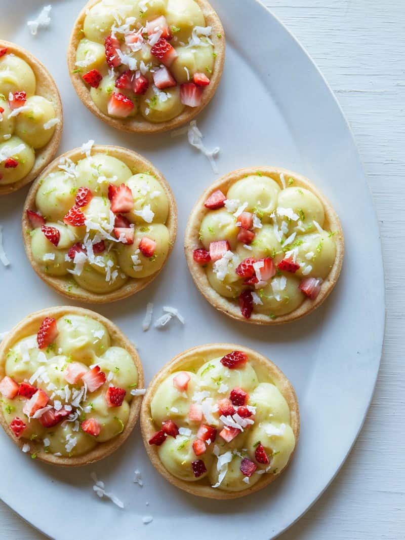 Several coconut lime tarts topped with sugar soaked strawberries.