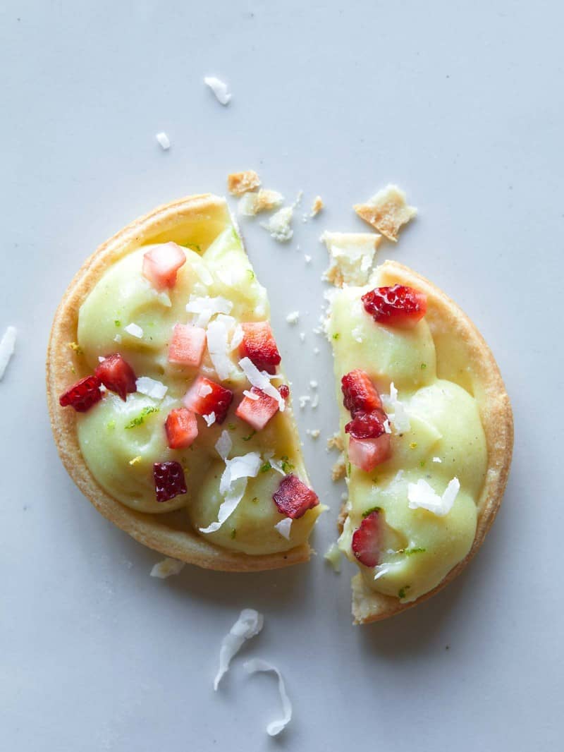 A close up of a coconut lime tart with sugar soaked strawberries, broken in half.