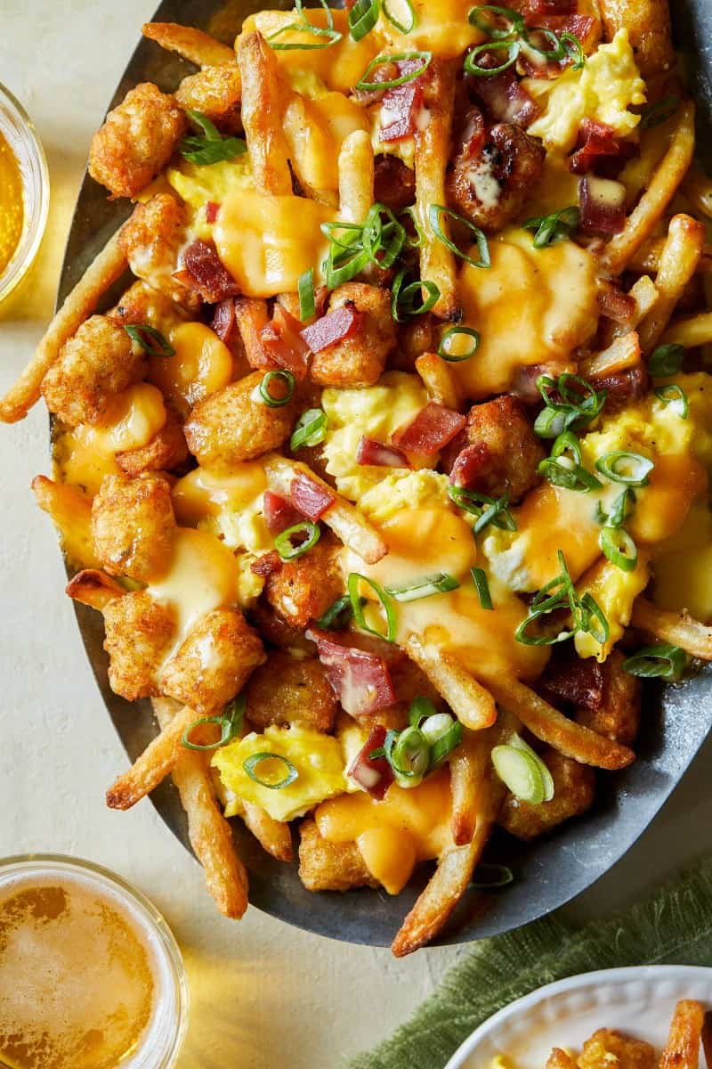 A close up of breakfast poutine with hollandaise sauce and drinks.