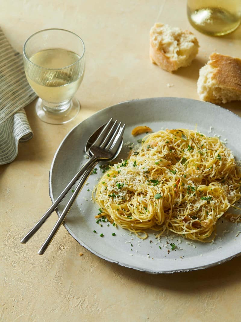 Garlic and herb capellini on a plate with a fork, spoon, bread, and a drink.