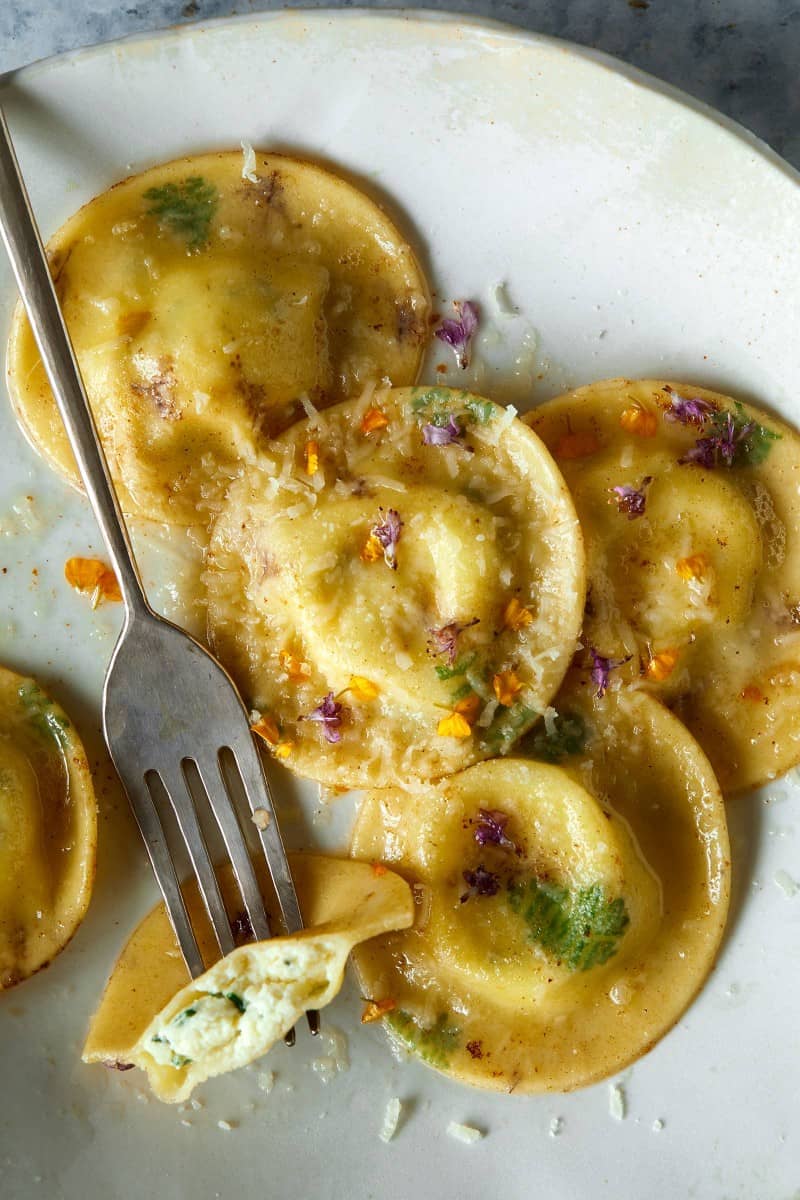A close up of cooked floral laced ravioli with cheesy herb ricotta filling and a fork.
