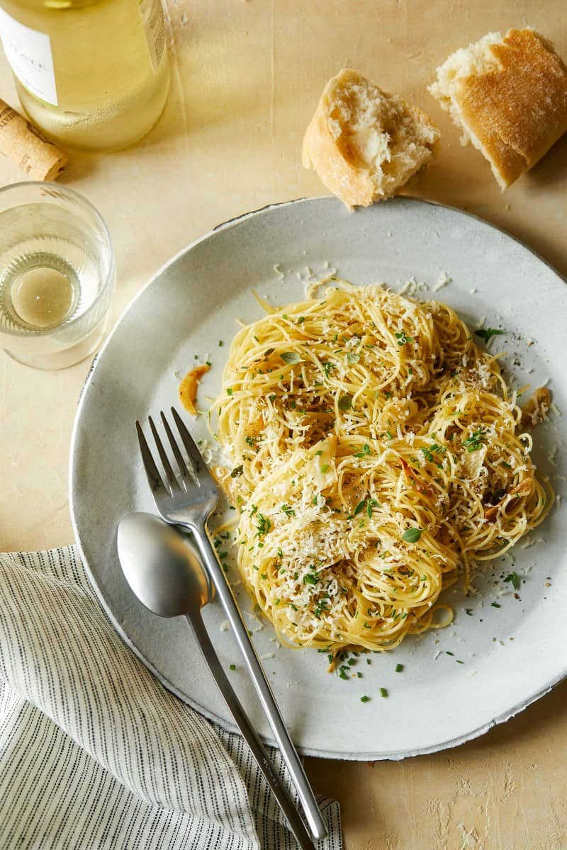 Garlic and herb capellini on a plate with a fork, spoon, bread, and a drink.