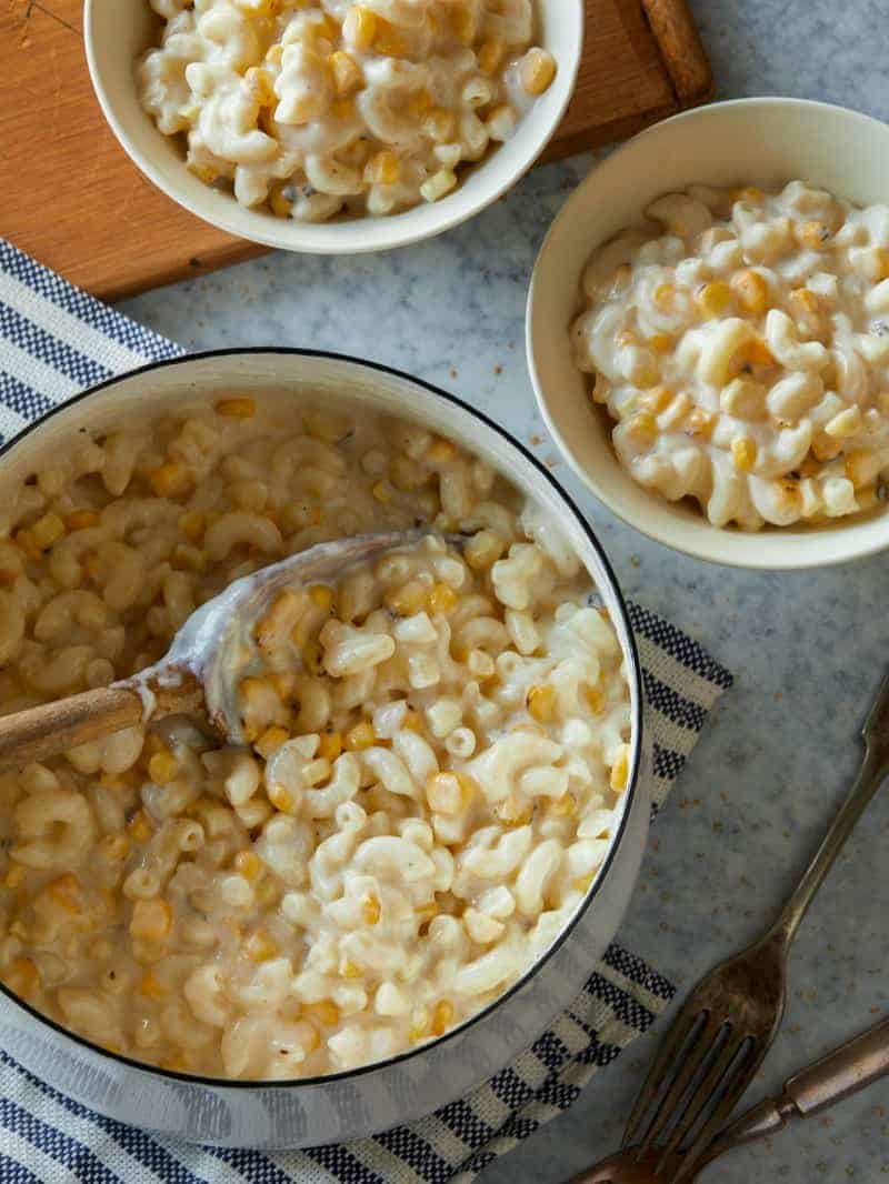 A pot and bowls of creamed corn mac and cheese with a serving spoon.