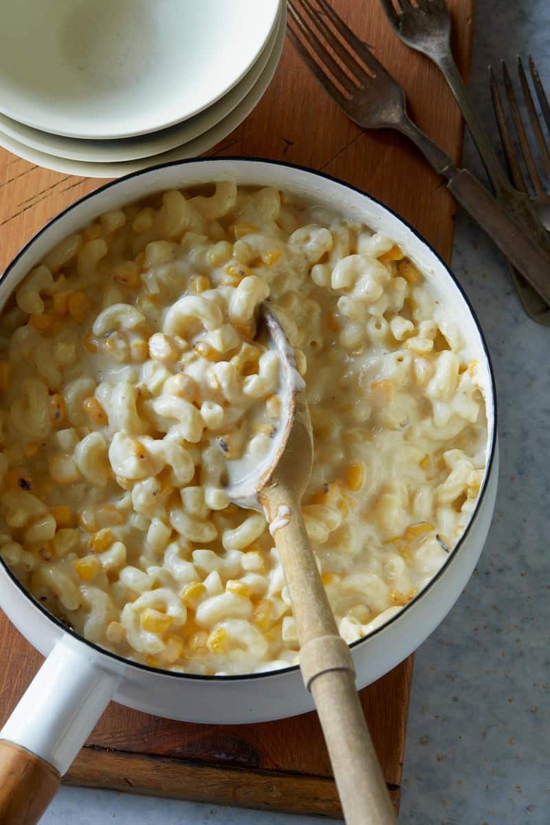 A pot of creamed corn mac and cheese with a wooden serving spoon.