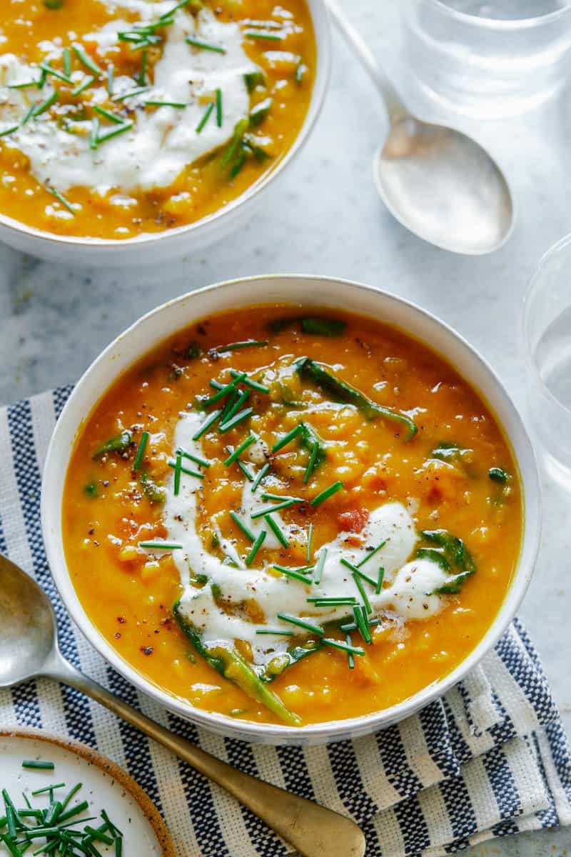 Bowls of vegan lentil and spinach soup topped with garlicky almond cream and spoons.