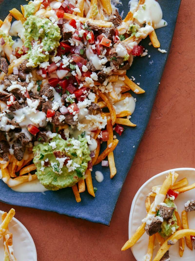 Carne asada fries on a blue platter with a serving on a small plate.