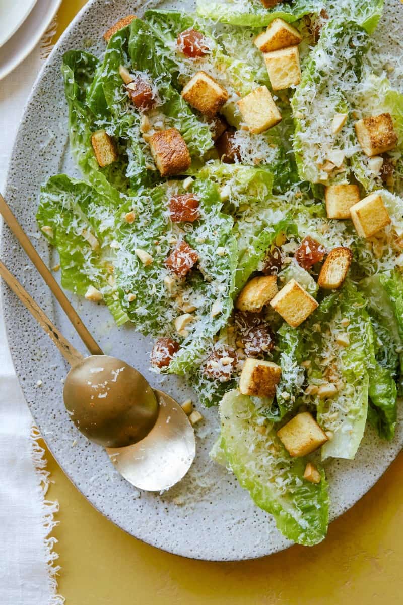 A close up of a simple salad with quince, manchego, and marcona almonds with serving spoons.