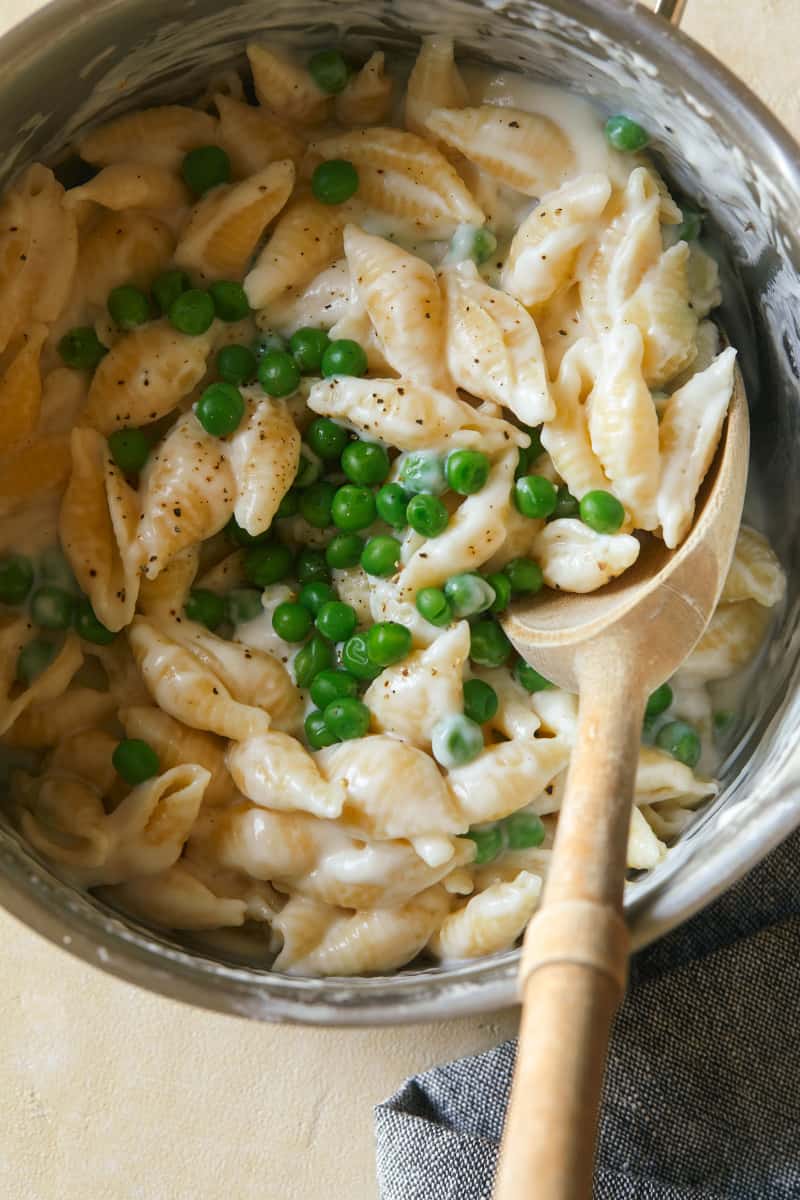 A close up of white cheddar mac, cheese, and sweet peas and a wooden spoon.