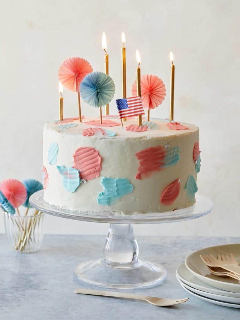 A whole 4th of July funfetti cake with candles and flags on a cake stand.
