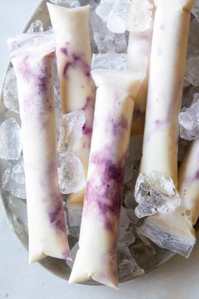 A close up of blackberry pineapple coconut ice pops on a plate with ice.