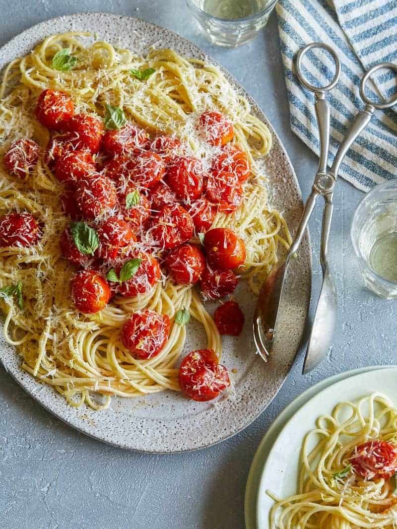 Butter roasted cherry tomato pasta on an oval platter with serving tongs.