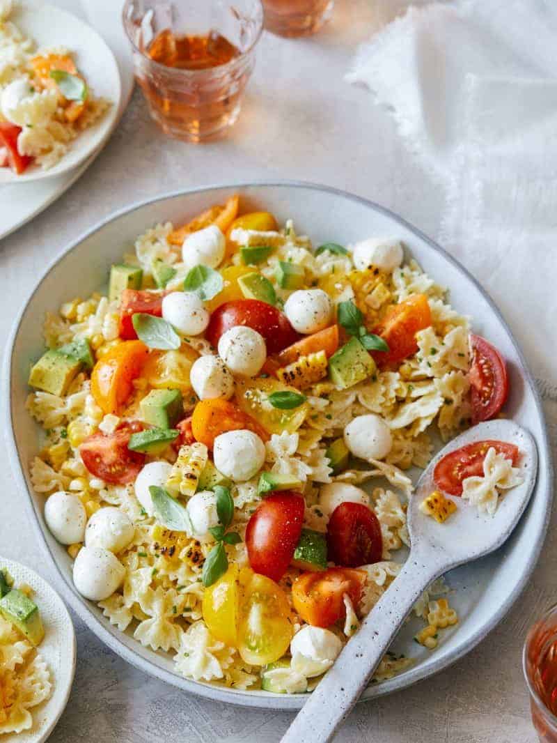 A plate of loaded pasta salad with a spoon.