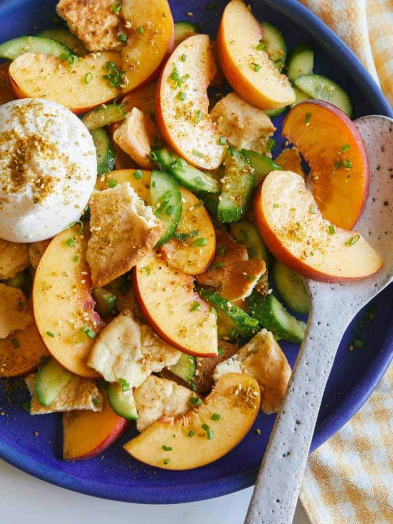 A close up of peach panzanella salad with a spoon.