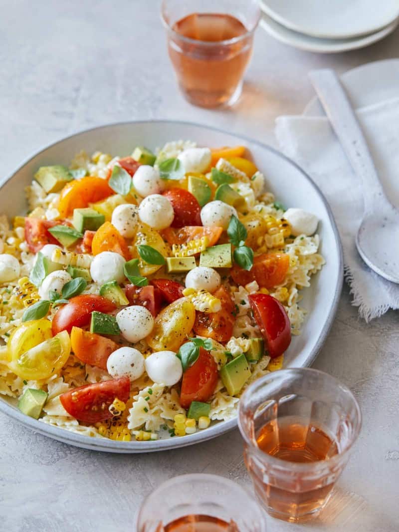 A plate of loaded pasta salad with a spoon and drinks.