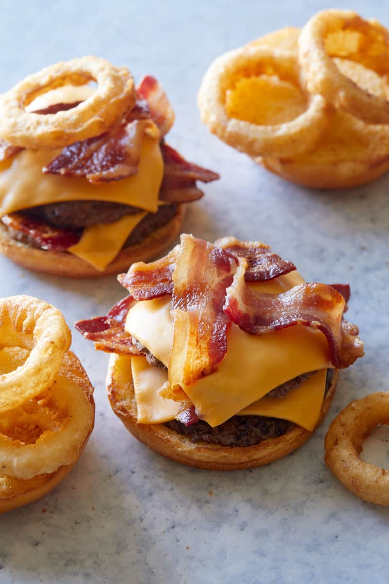 A close up of open bacon western double cheeseburgers with onion rings.