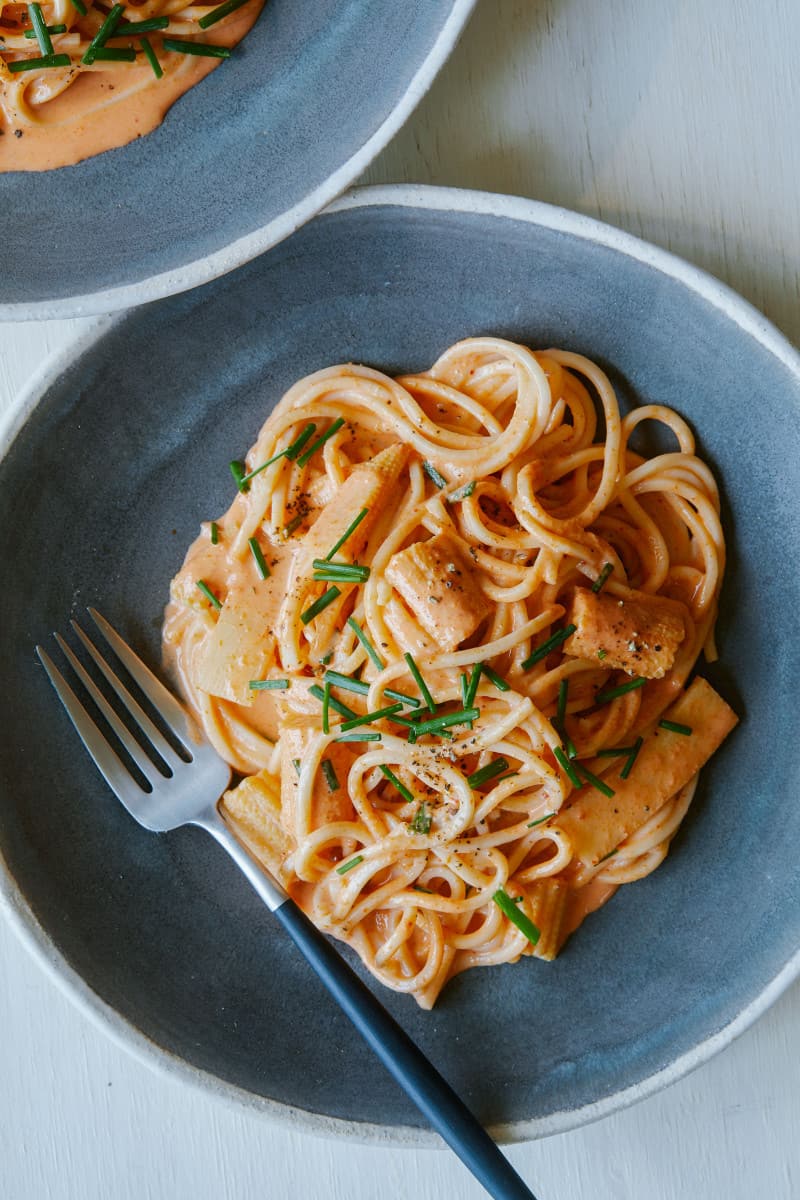 A blue bowl of red curry noodles with a fork.