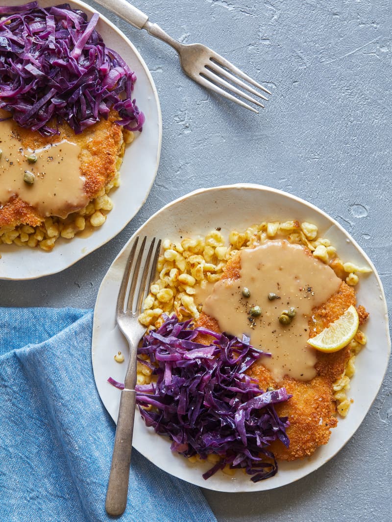 Plates of schnitzel over buttered spaetzle with sweet and sour cabbage, lemon wedges and forks.