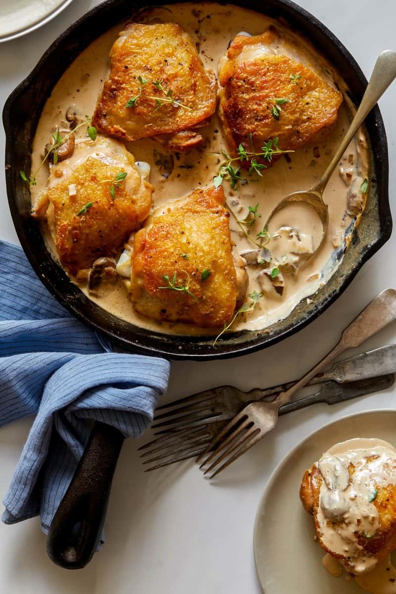 Crispy chicken thighs with a creamy mushroom sauce in a skillet with forks.
