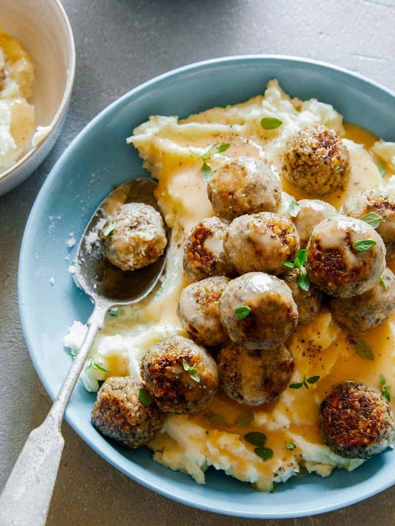 Vegan swedish meatballs over mashed potatoes and gravy with a spoon.