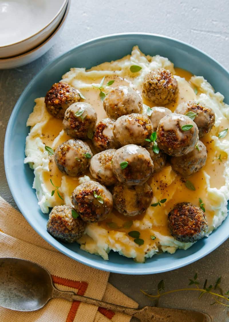 Vegan swedish meatballs over mashed potatoes and gravy in a blue bowl.