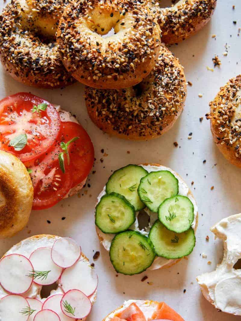 Everything bagels, some sliced and topped with cream cheese and veggies.