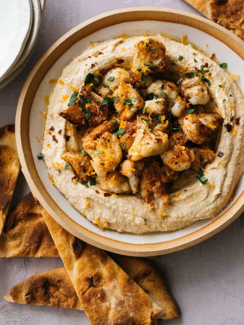 A close up of spicy roasted cauliflower over hummus in a bowl with pita chips.