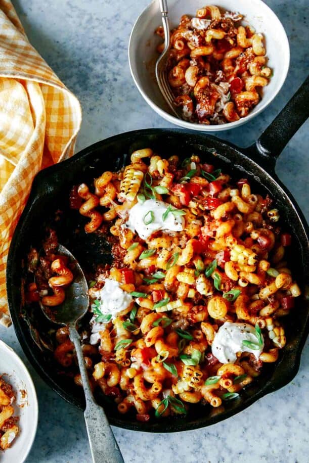 Taco pasta in a skillet with a spoon and a serving in a bowl.