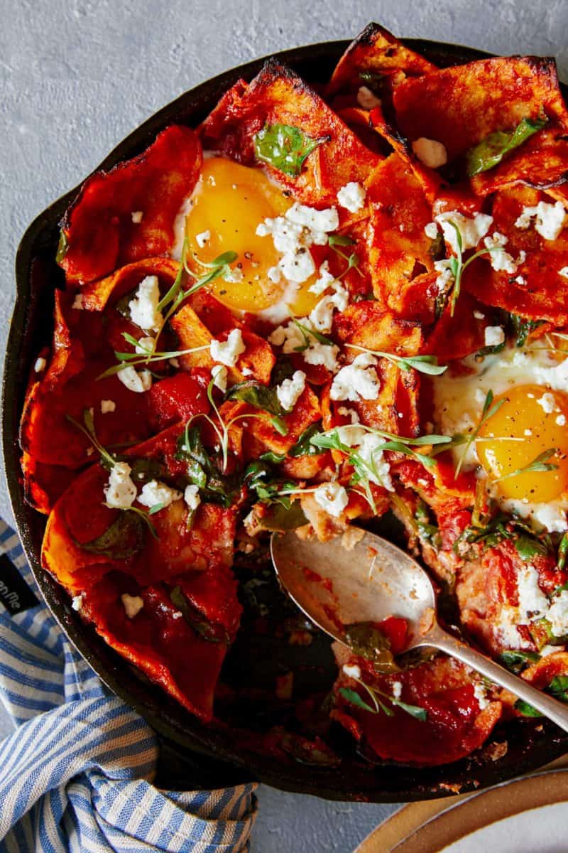 A close up of shakshuka chilaquiles in a pan with a spoon.