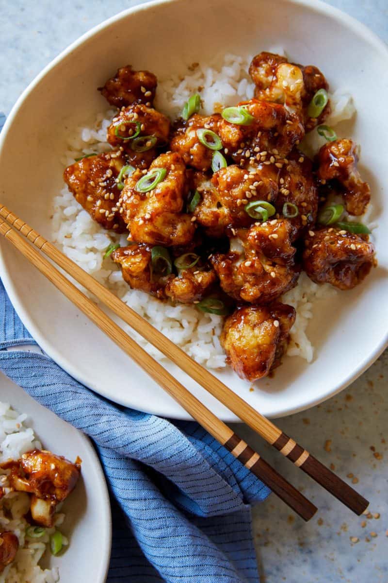 A close up of a bowl of honey garlic cauliflower over white rice with chopsticks.