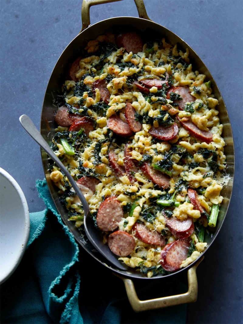 Sausage kale and spaetzle pesto bake in a pan with a spoon.