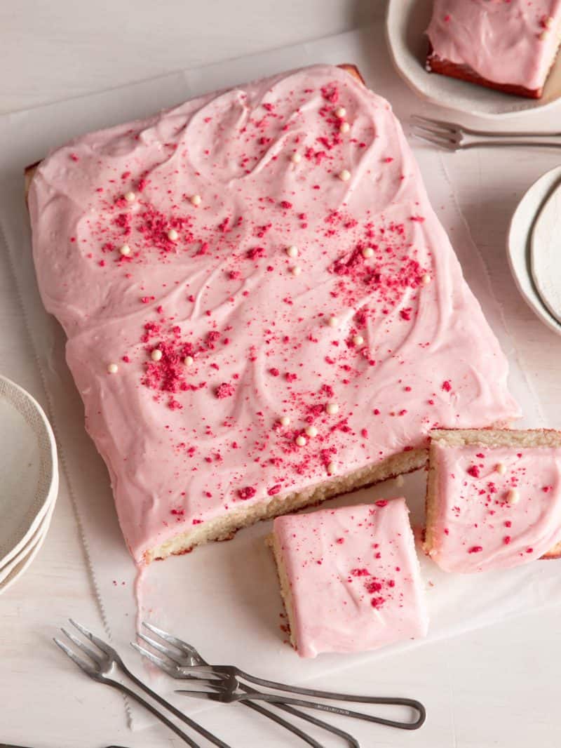 A sliced vanilla bean sheet cake with strawberry frosting and forks.