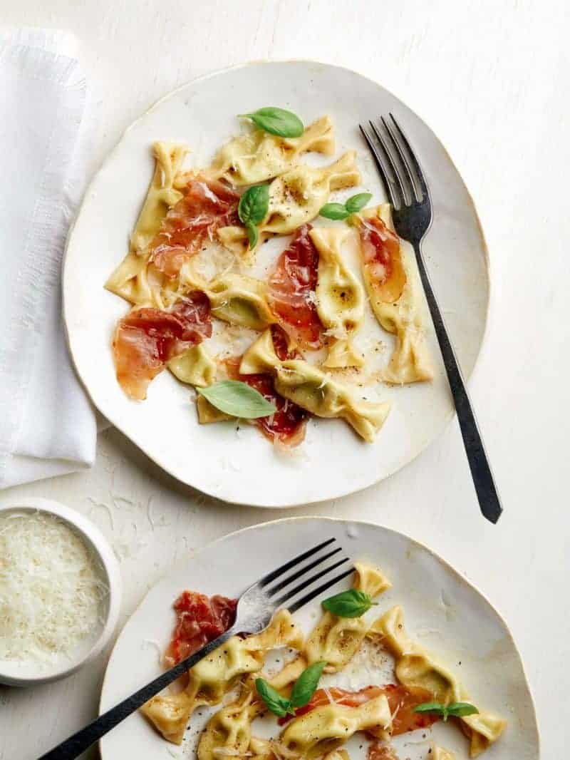 Plates of sweet pea caramelle with prosciutto and forks.