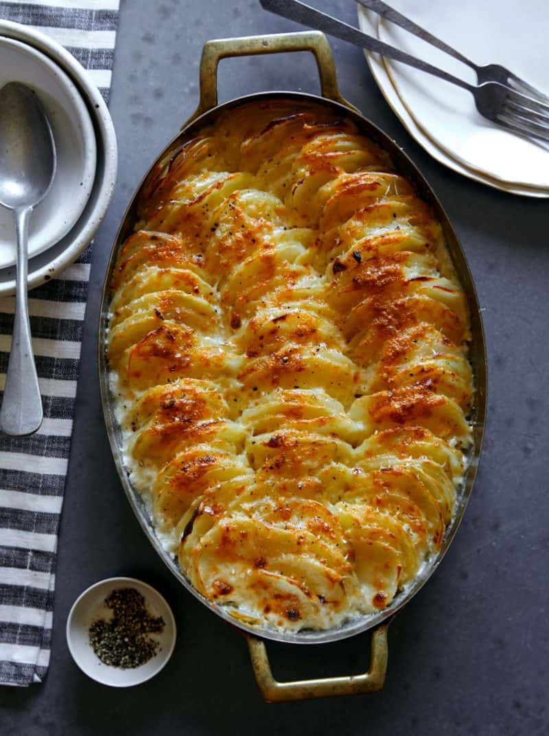 Cheesy Garlic Potato gratin in an oval baking dish with a spoon.