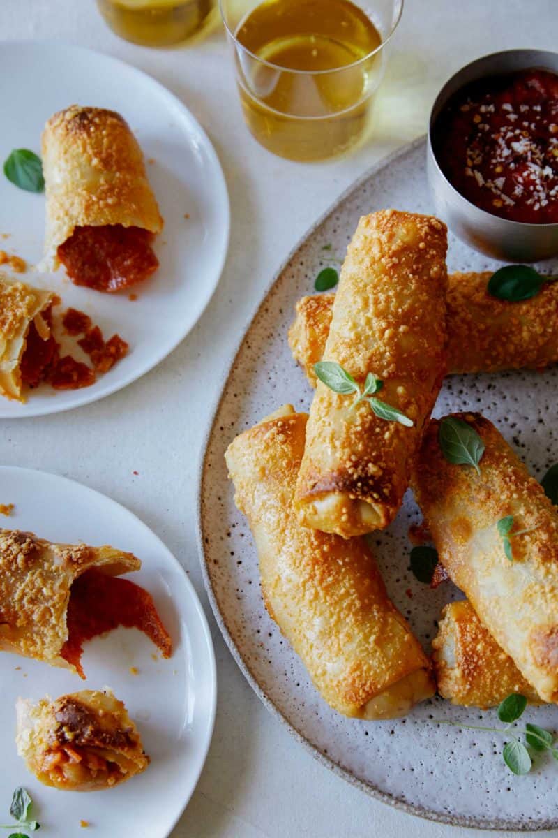 A close up of crispy baked pepperoni pizza egg rolls with sauce on the side.
