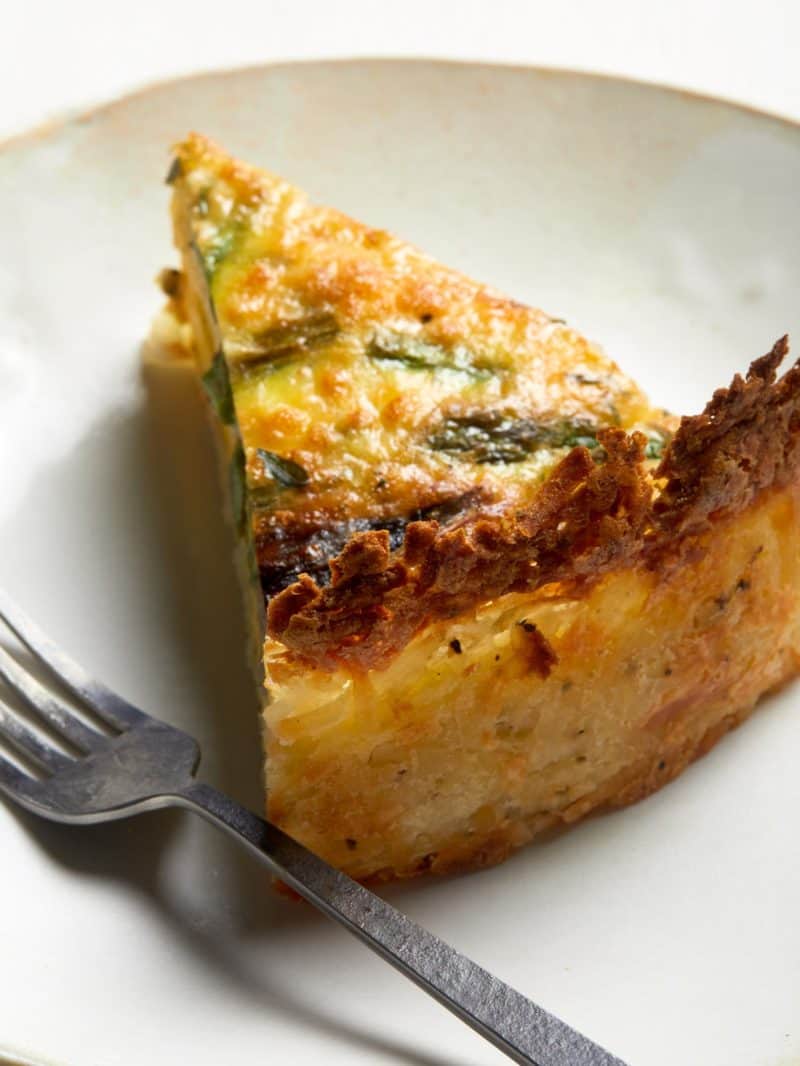 A close up of a slice of spring quiche with hash brown crust with a fork.