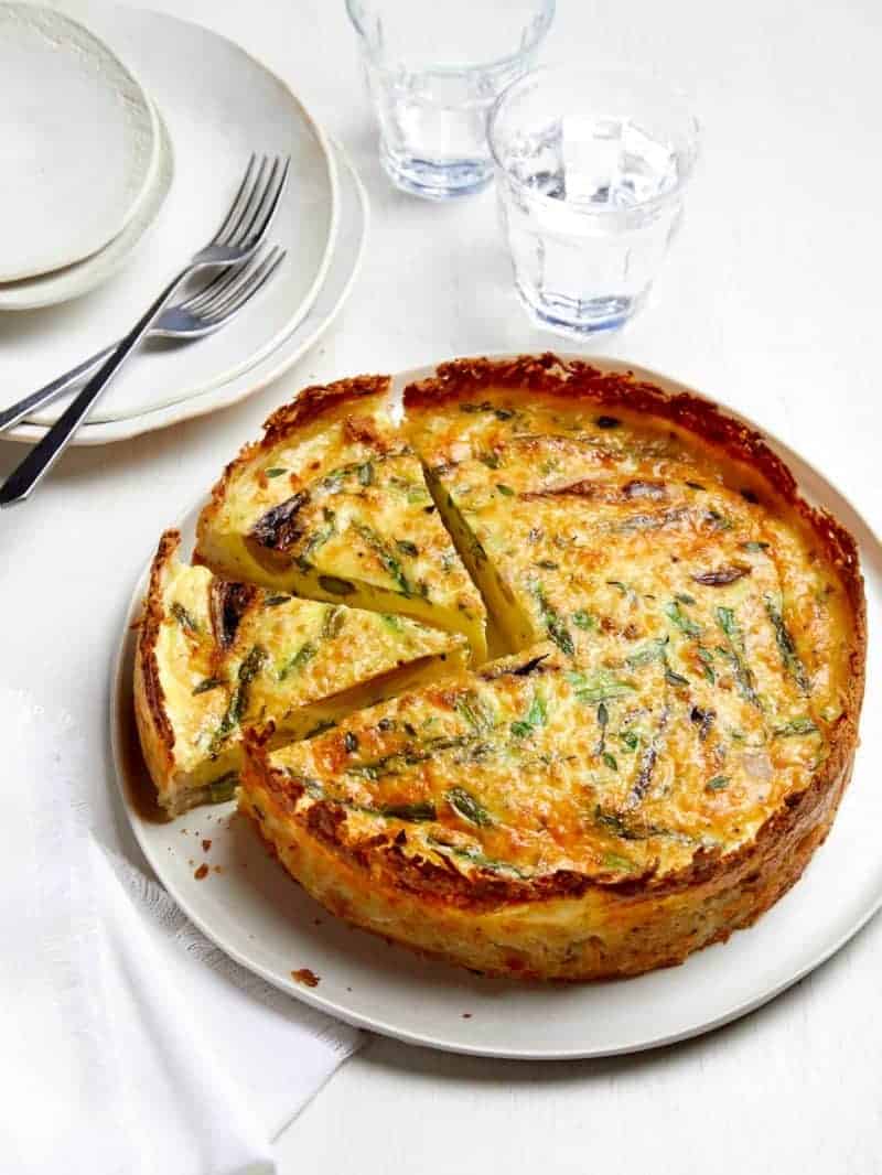 A whole sliced spring quiche with hash brown crust with extra plates and forks.