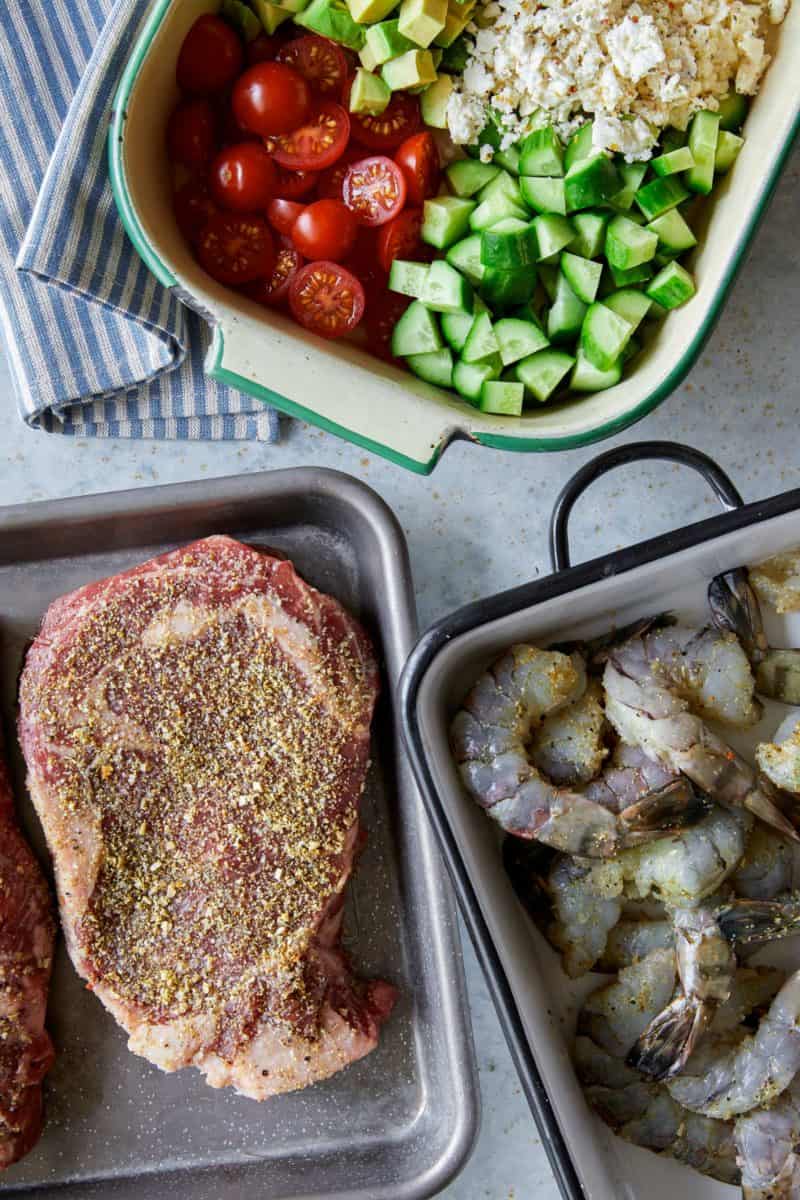 Raw shrimp and steak next to uncooked veggies.