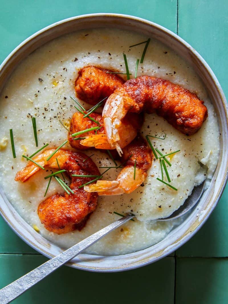 A close up of a bowl of shrimp over cheesy corn grits with a spoon.