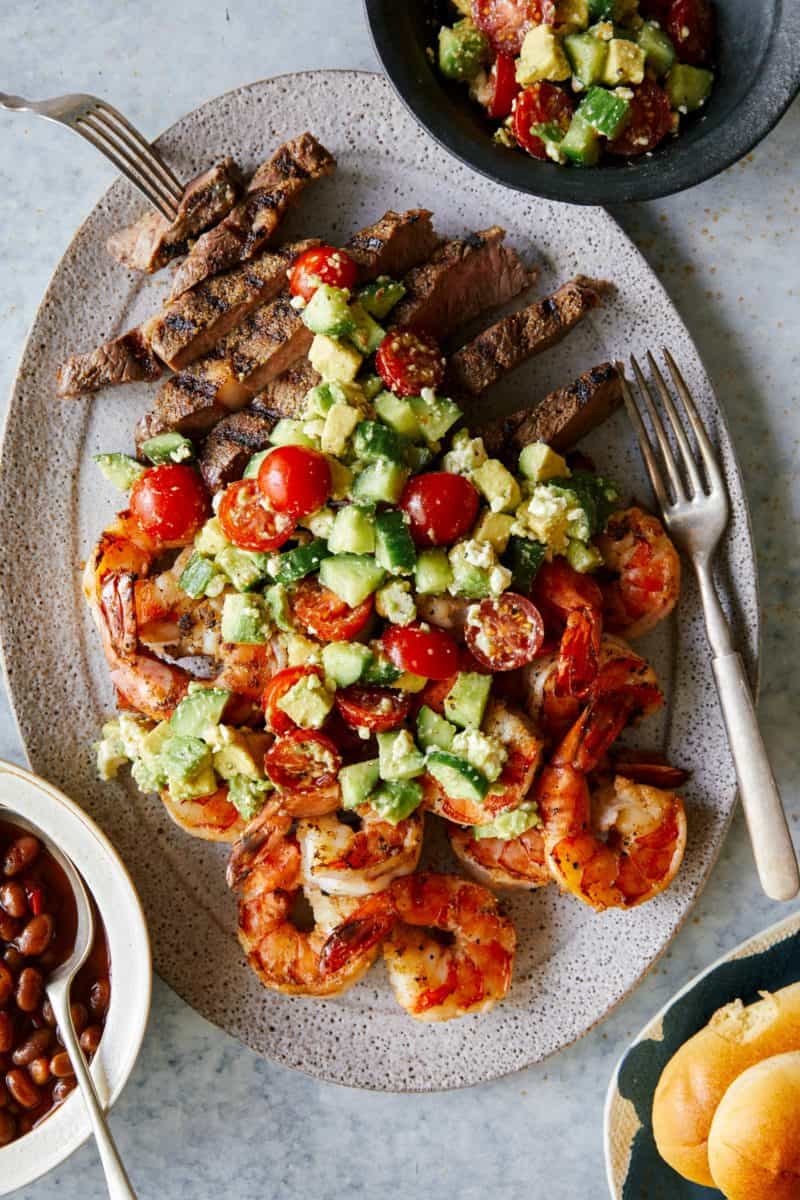 Grilled shrimp and steak platter topped with veggies with a fork.
