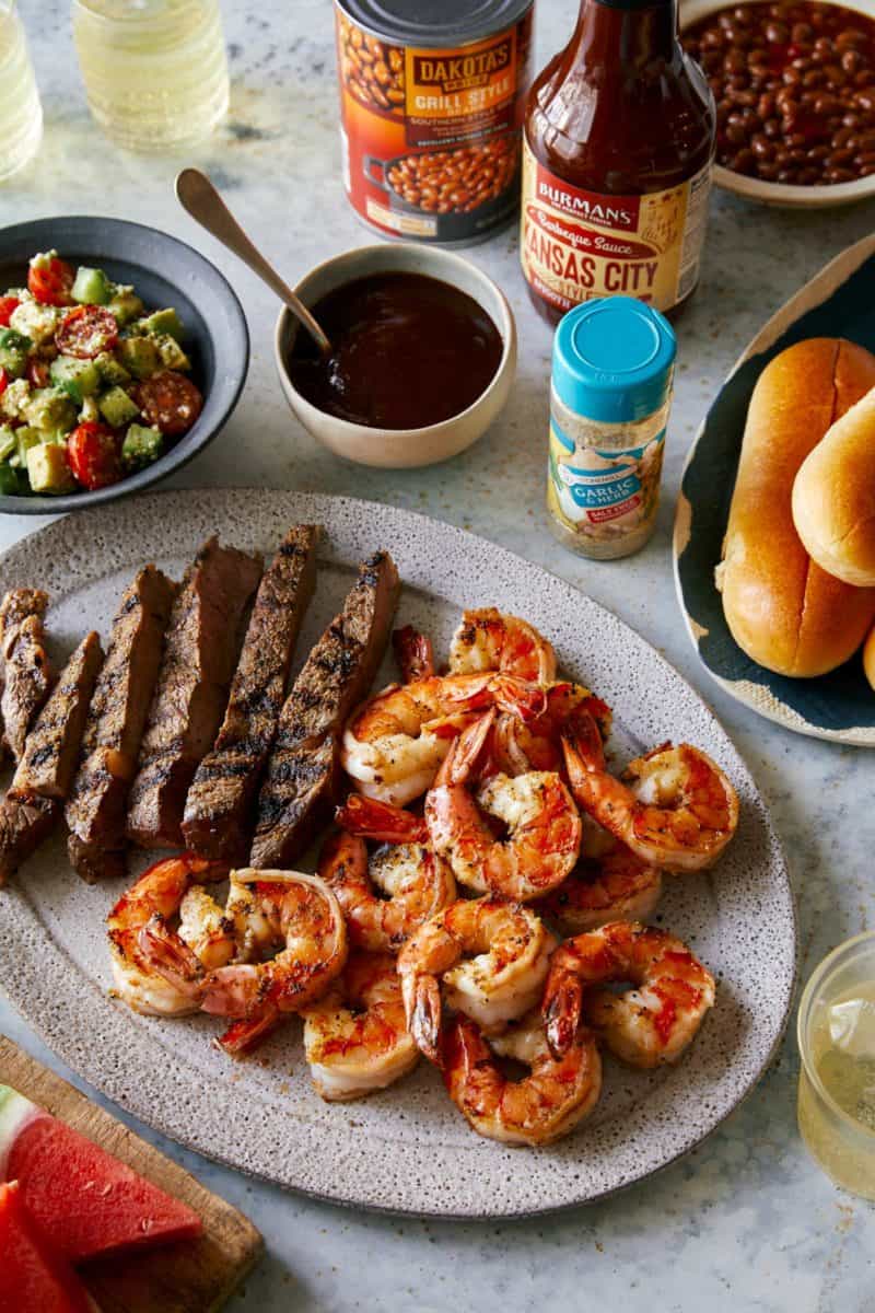 Grilled shrimp and steak platter with sides of salad, sauces and rolls.