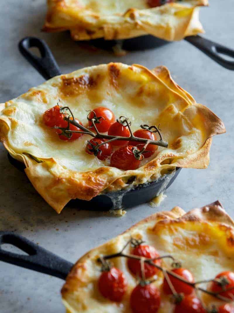 A close up of an creamy turkey kale skillet lasagne with a vine of cherry tomatoes.